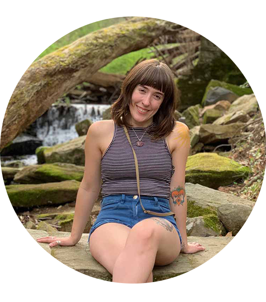 A portrait of Yesie Lauren sitting on rocks with a forest background